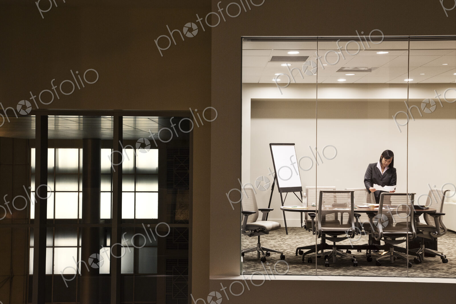 A view looking into a conference room at night of an Asian businesswoman.