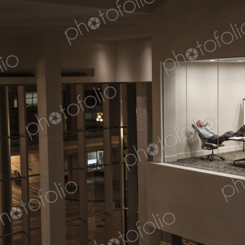 A view looking into a conference room at night with a single businessman at a…