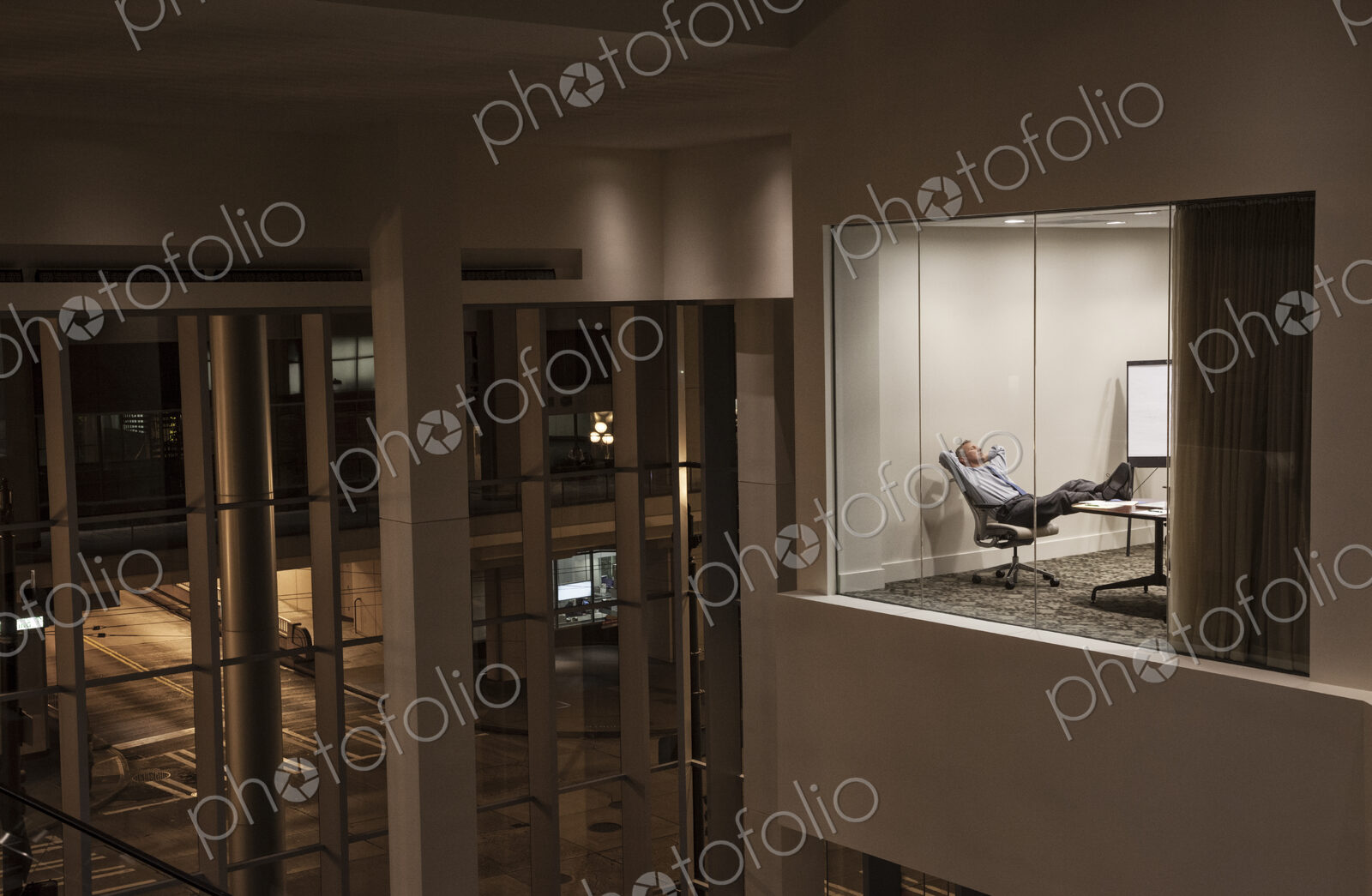 A view looking into a conference room at night with a single businessman at a…