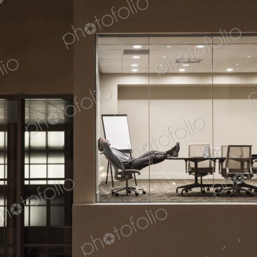 A view looking into a conference room at night with a single businessman at a…