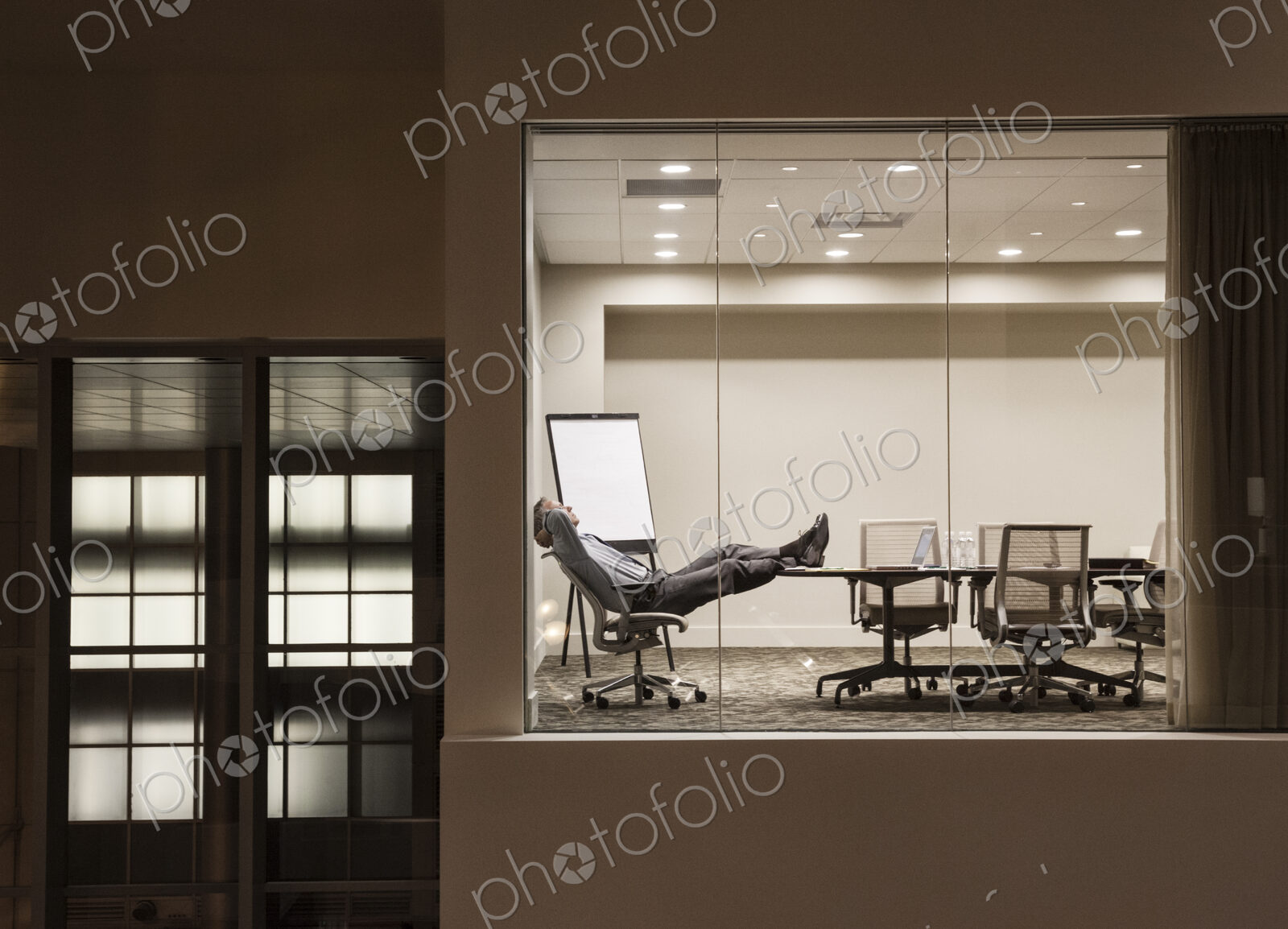 A view looking into a conference room at night with a single businessman at a…