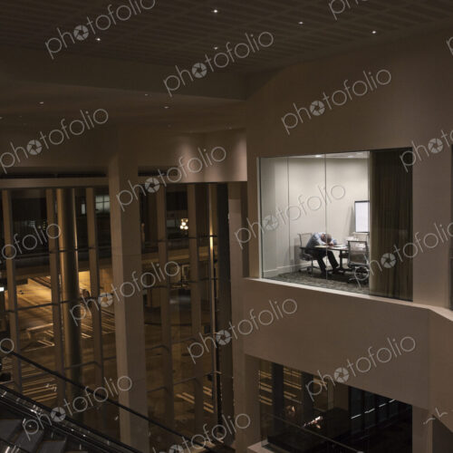 A view looking into a conference room at night with a single businessman at a…