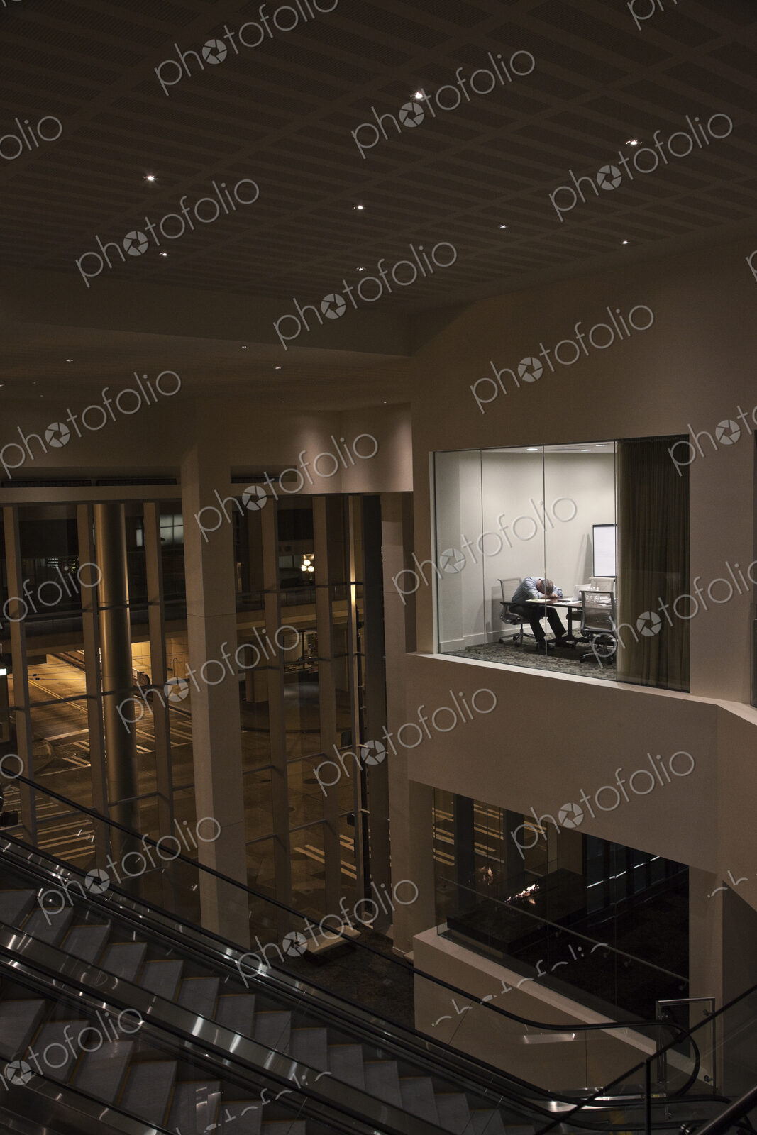 A view looking into a conference room at night with a single businessman at a…