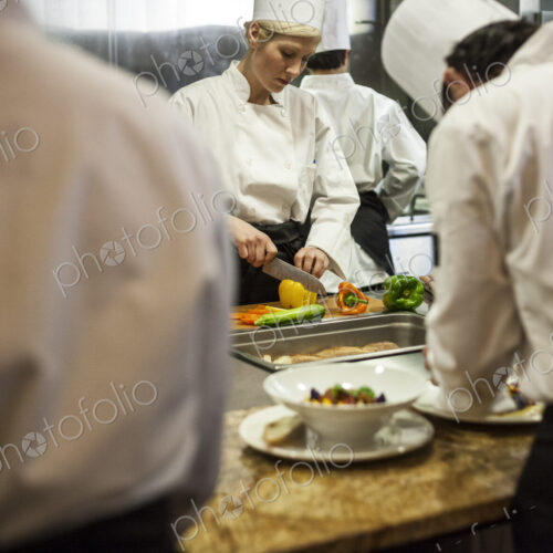 A view looking through kitchen employees of a female chef cutting vegetables. A view looking through kitchen employees of a female chef cutting vegetables.