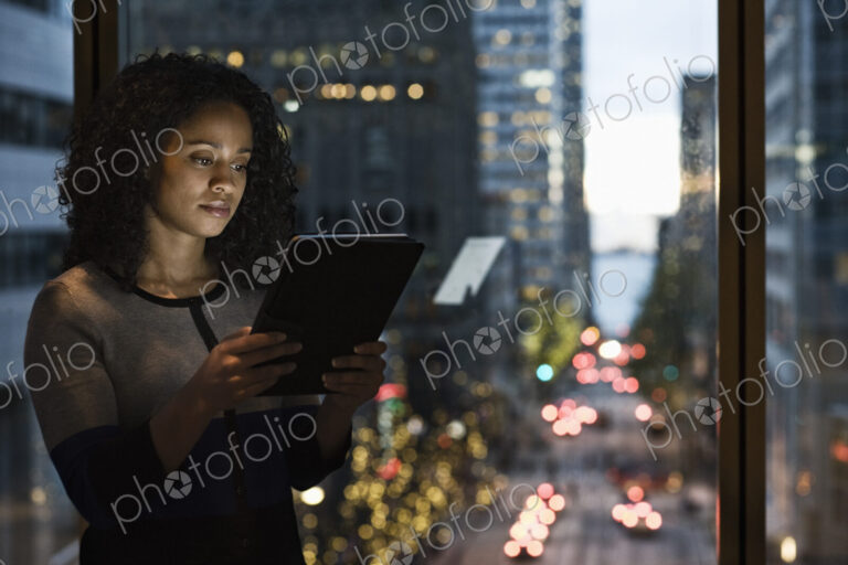 A view of a black businesswoman working on a digital tablet by a window with a city view