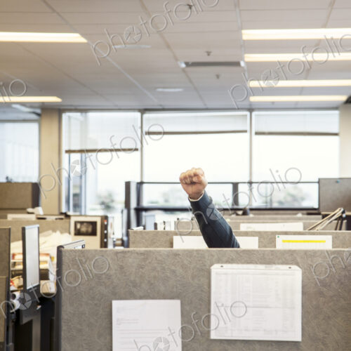A view of cubicles in an office with a person raising their fist.
