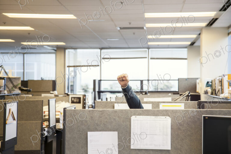 A view of cubicles in an office with a person raising their fist.