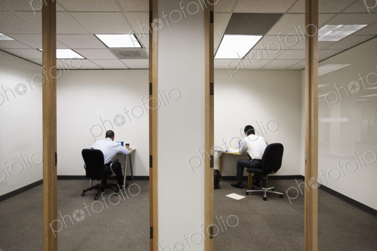 A view of two businessmen working on opposite sides of a wall in two different office…