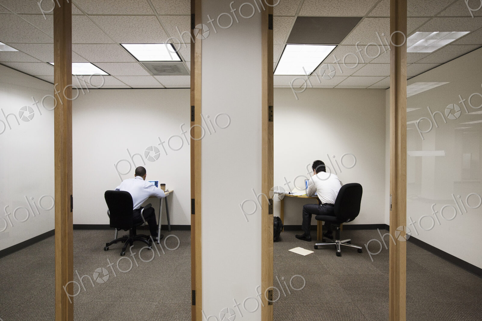 A view of two businessmen working on opposite sides of a wall in two different office…