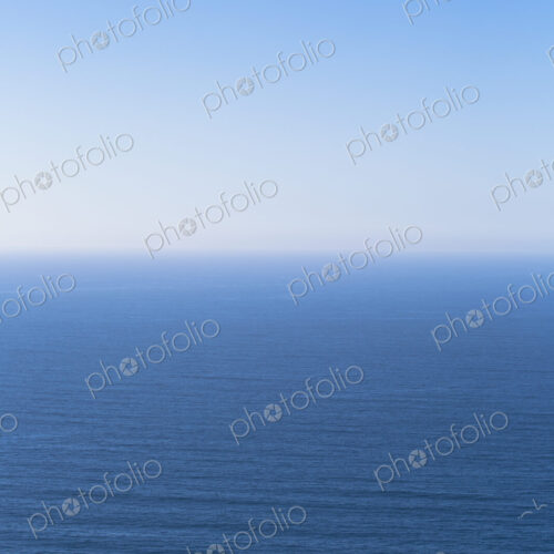 A view over the Pacific Ocean and a calm sea, merging into the blue sky.