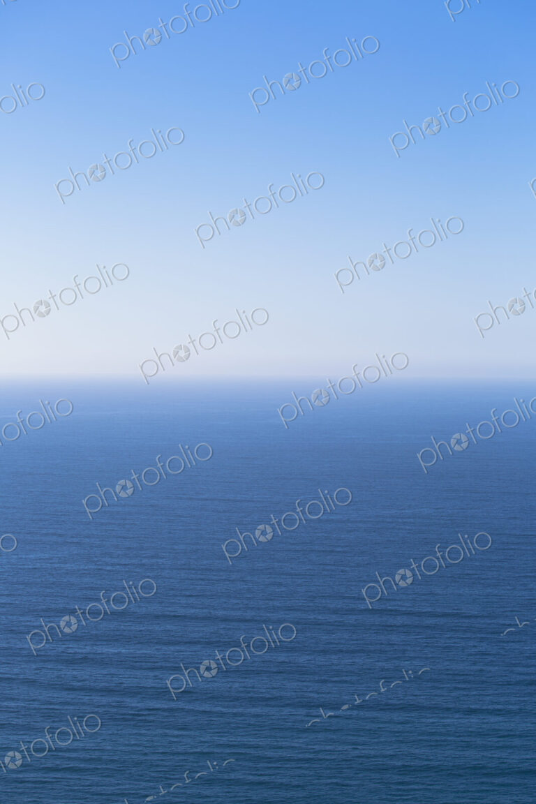 A view over the Pacific Ocean and a calm sea, merging into the blue sky.