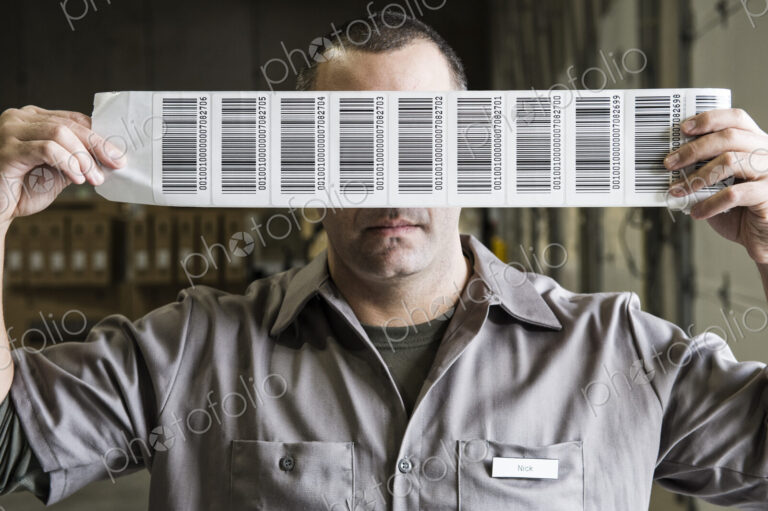 A warehouse worker holding up a sheet of bar code shipping lables in a distribution…