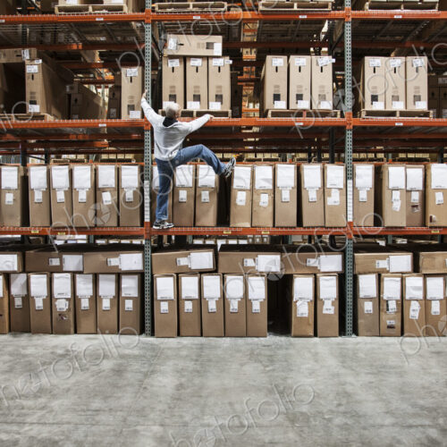 A warehouse worker trying to climb a rack of products in a distribution warehouse. A warehouse worker trying to climb a rack of products in a distribution warehouse.