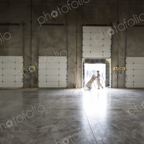 A warehouse worker with a hand truck at a loading dock door in a warehouse. A warehouse worker with a hand truck at a loading dock door in a warehouse.