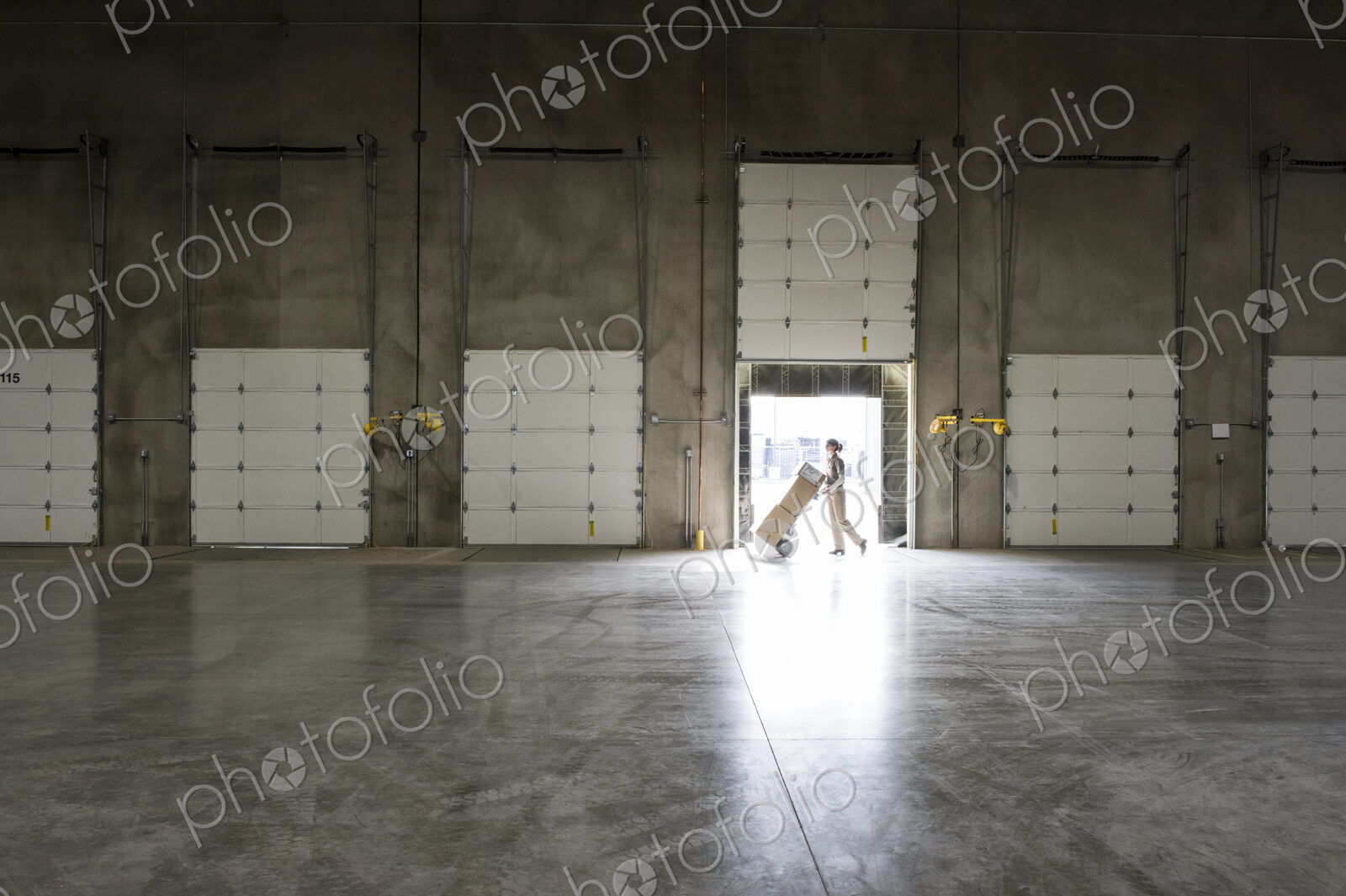 A warehouse worker with a hand truck at a loading dock door in a warehouse.