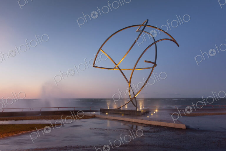 A weather storm, waves crashing over the waterfront promenade and metal sculpture