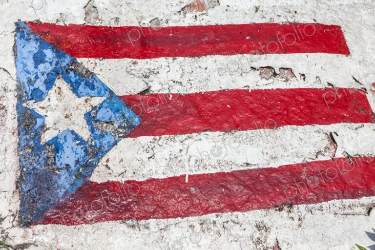 A weathered painting of the Puerto Rican flag is shown on a textured rock surface at…
