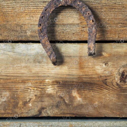 A weathered, rusted horseshoe hangs upside down on an aged wooden plank wall,…