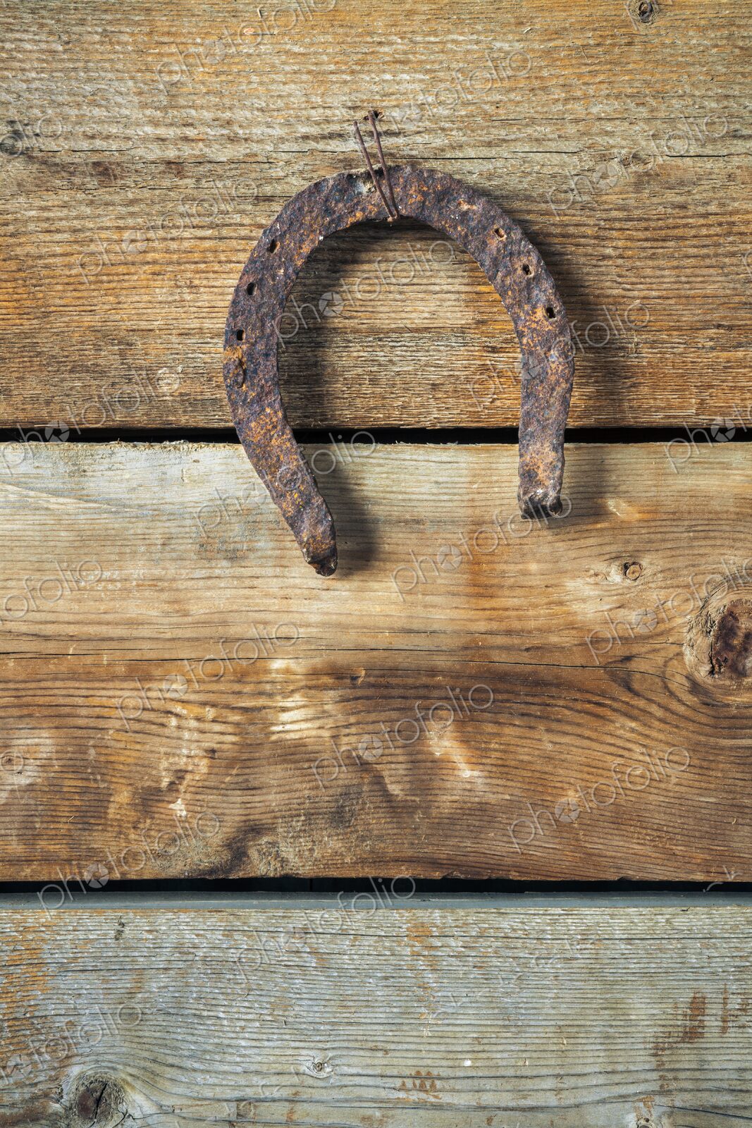 A weathered, rusted horseshoe hangs upside down on an aged wooden plank wall,…