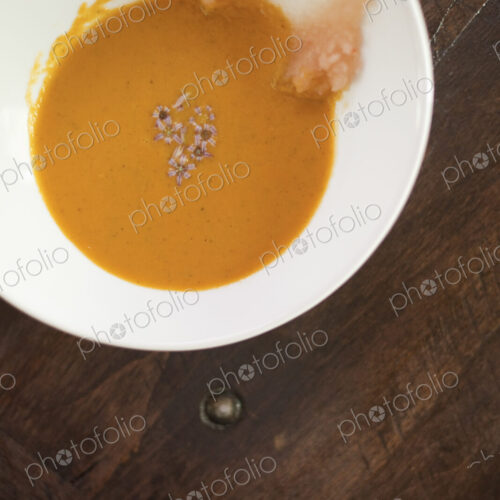 A white china bowl with a creamy soup and garnish, viewed from above. A rouille puree…