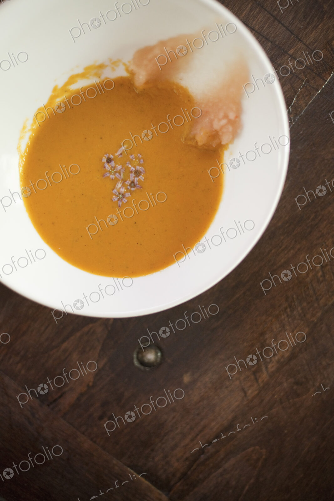 A white china bowl with a creamy soup and garnish, viewed from above. A rouille puree…