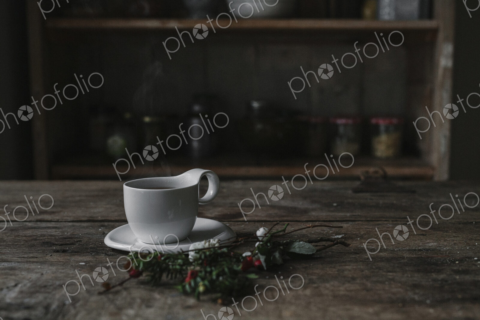 A white china cup and saucer on a kitchen table and a twig of pine and berries.