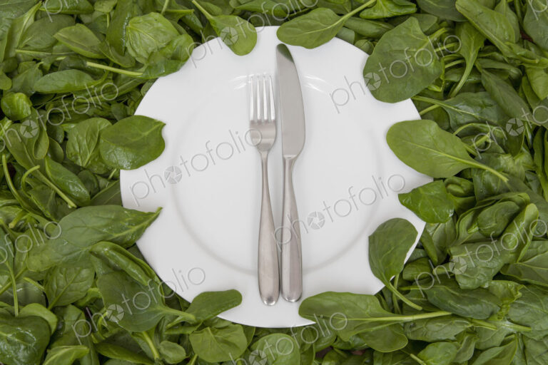 A white china plate with a knife and fork, resting on edible leaves. The concept of…