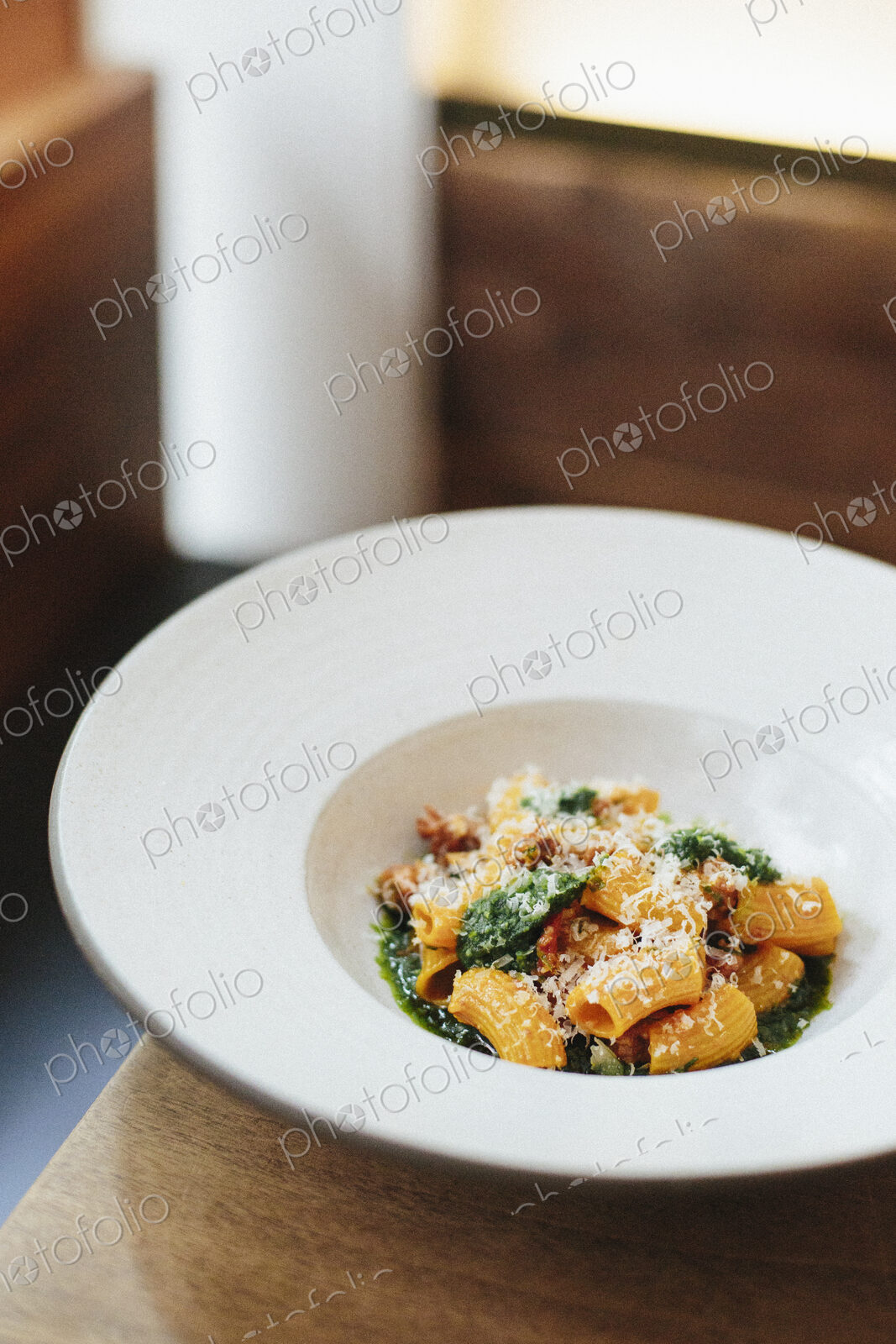 A white dish with pasta and a vegetable sauce and shavings of parmesan.