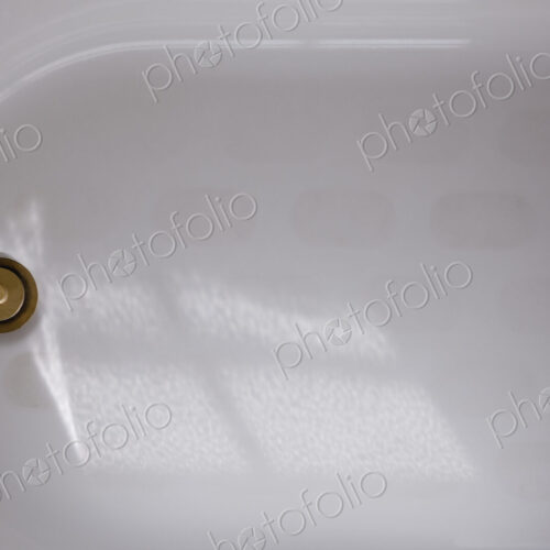 A white enamel bathtub with a brass plug or drain cover, overhead view. A white enamel bathtub with a brass plug or drain cover, overhead view.