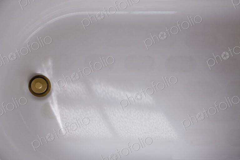 A white enamel bathtub with a brass plug or drain cover, overhead view.