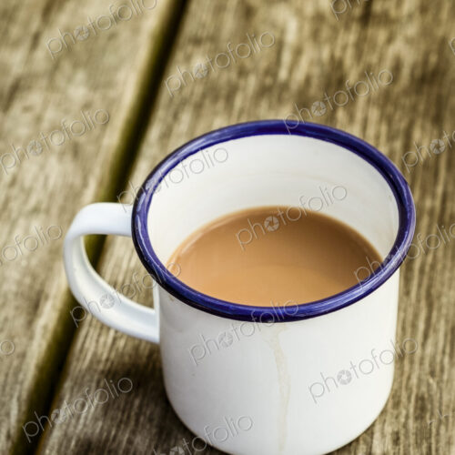 A white enamel mug of tea with a blue rim on a wooden table.
