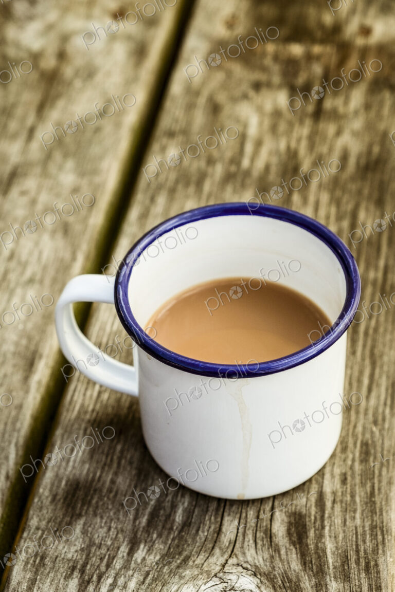 A white enamel mug of tea with a blue rim on a wooden table.