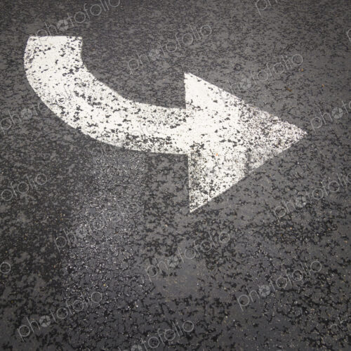 A white painted curving arrow symbol, a road marking on a road surface. A white painted curving arrow symbol, a road marking on a road surface.