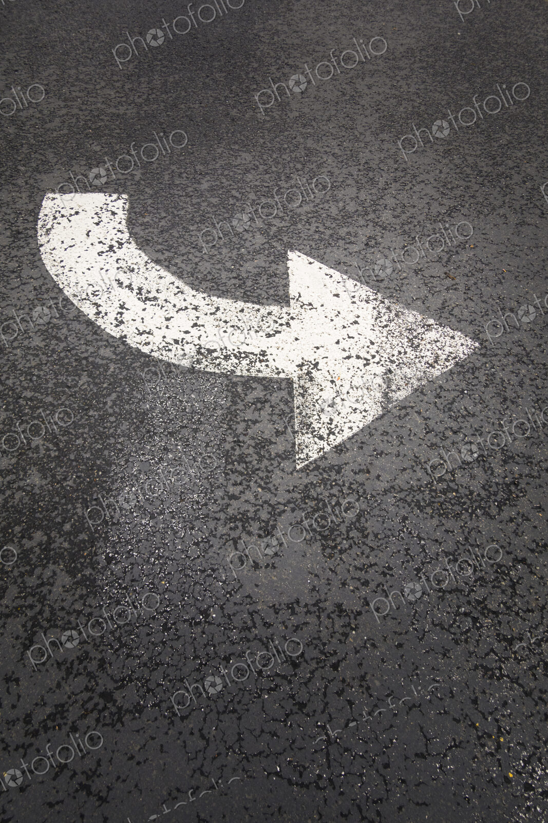 A white painted curving arrow symbol, a road marking on a road surface.