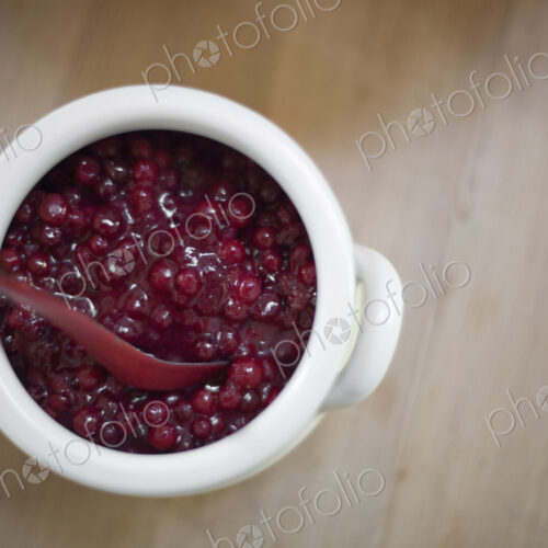 A white pottery bowl, full of fresh cranberries with a matching spoon. A relish or sauce.