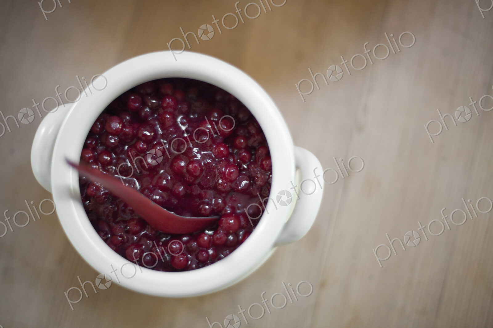 A white pottery bowl, full of fresh cranberries with a matching spoon. A relish or sauce.