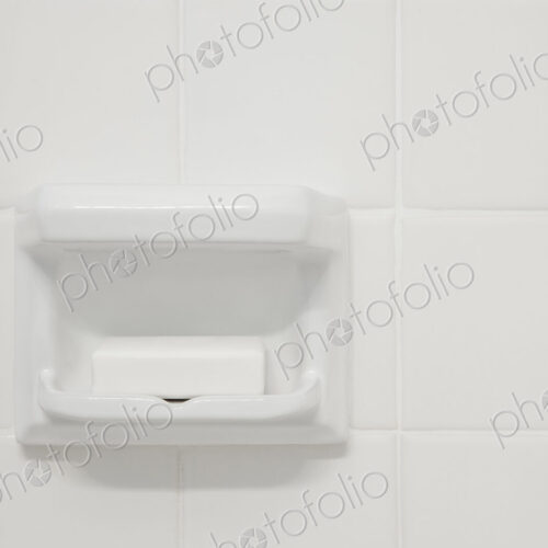 A white tiled wall of a bathroom or shower room,with a shaped porcelain recess. A…