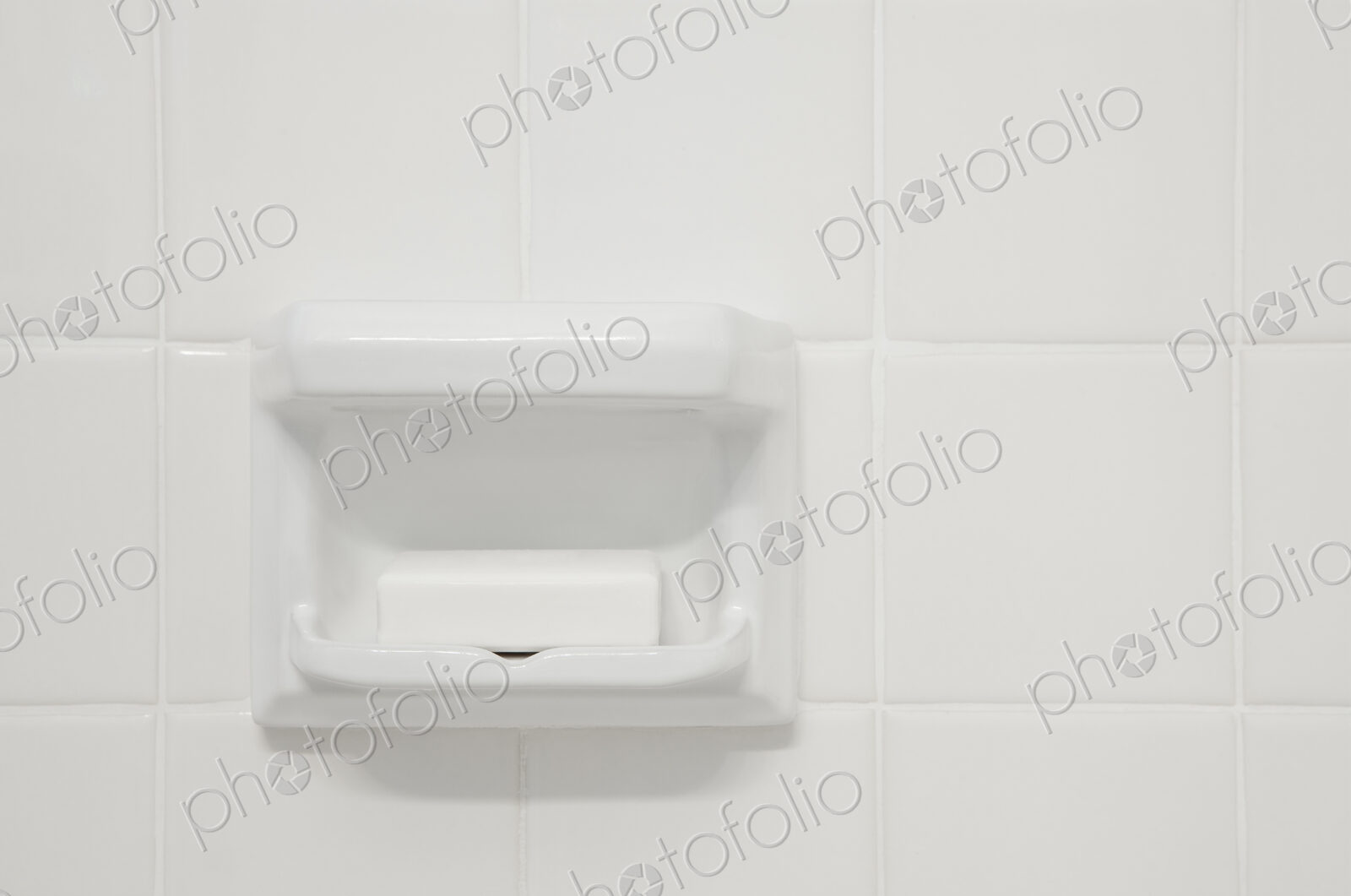 A white tiled wall of a bathroom or shower room,with a shaped porcelain recess. A…