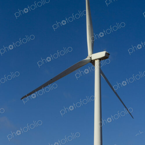A wind turbine with rotating arms against a blue sky. A wind turbine with rotating arms against a blue sky.