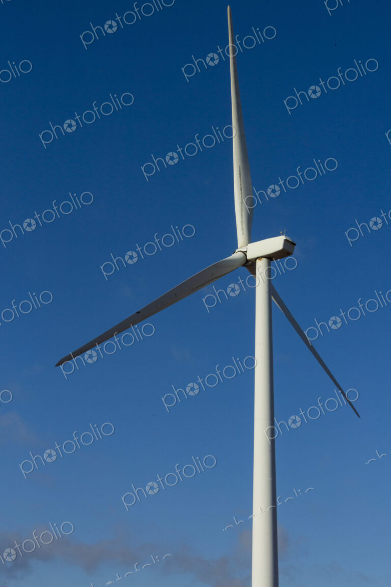 A wind turbine with rotating arms against a blue sky.