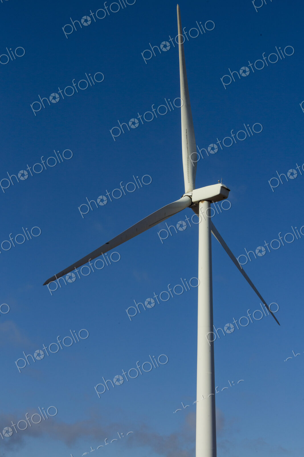 A wind turbine with rotating arms against a blue sky.