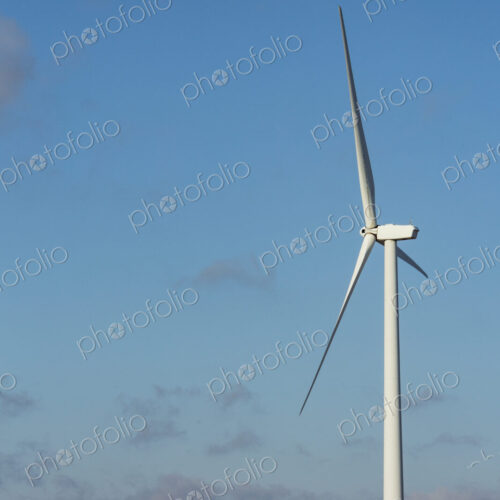 A wind turbine with rotating arms against a blue sky. A wind turbine with rotating arms against a blue sky.