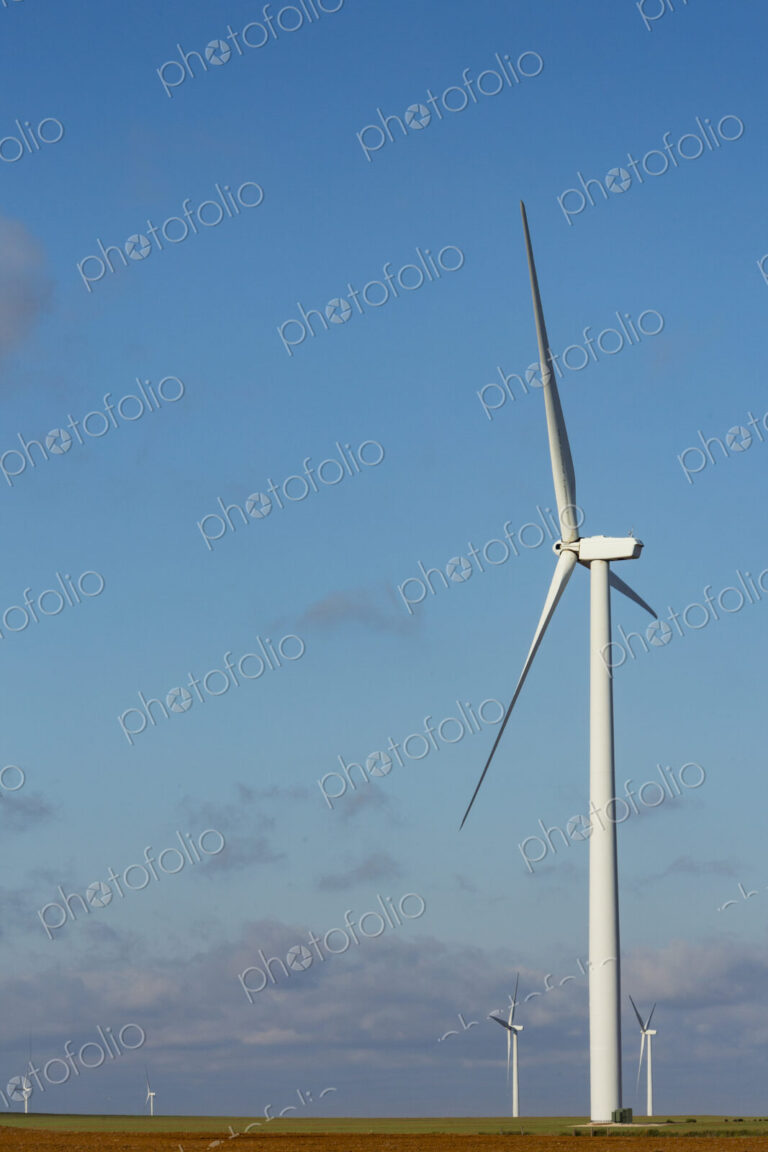 A wind turbine with rotating arms against a blue sky.