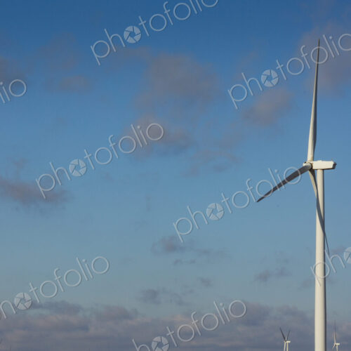 A wind turbine with rotating arms against a blue sky. A wind turbine with rotating arms against a blue sky.