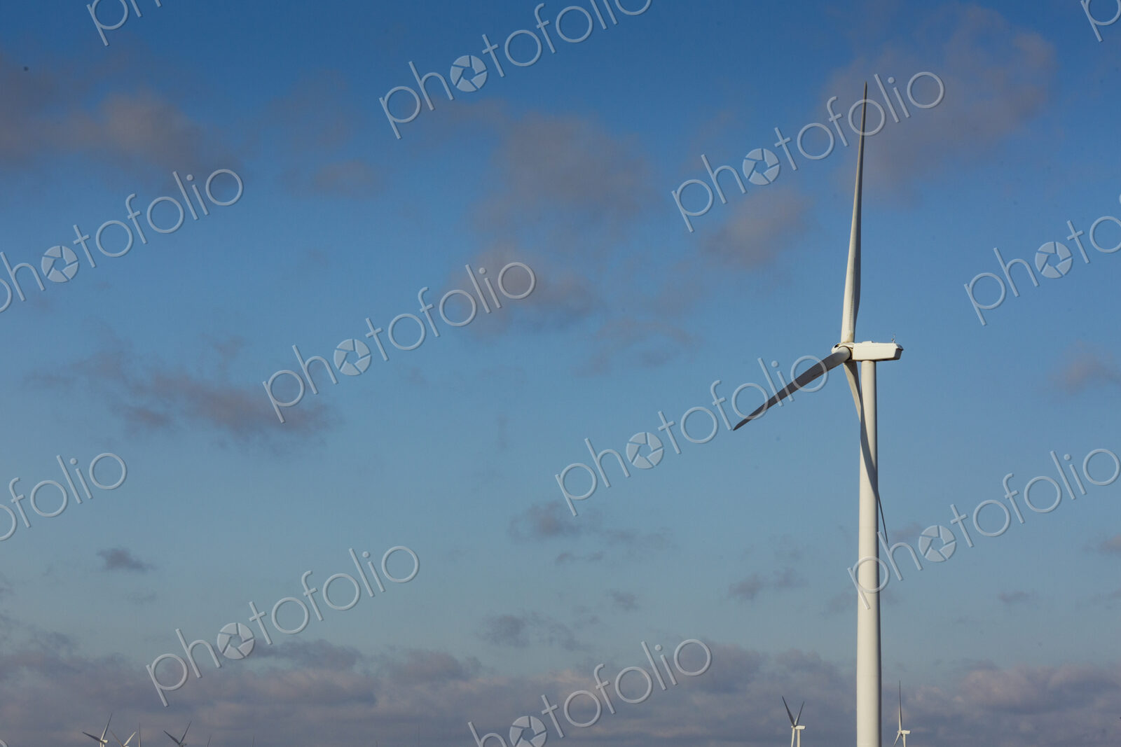 A wind turbine with rotating arms against a blue sky.