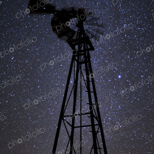 A windmill tower at night, against a starry sky, low angle view. A windmill tower at night, against a starry sky, low angle view.