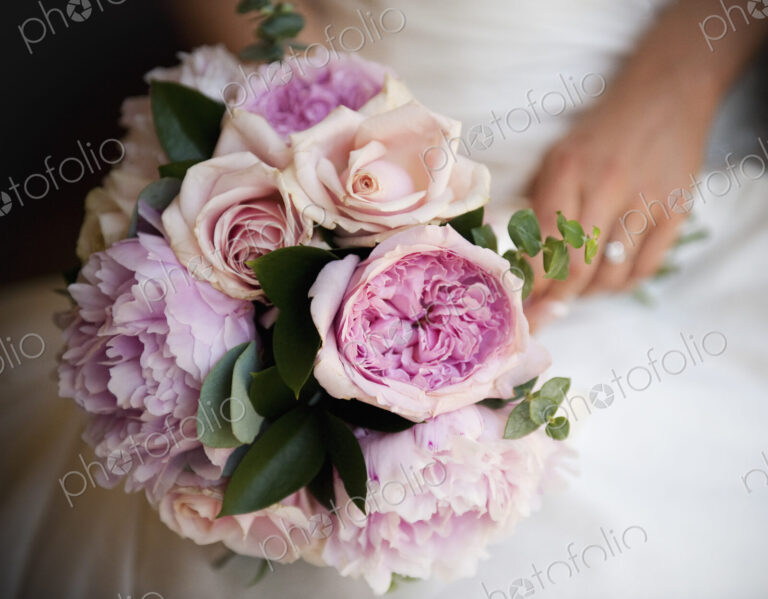 A woman, a bride holding a bridal bouquet of pastel coloured pale pink roses and…