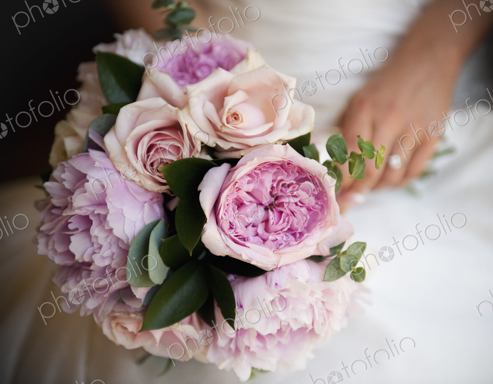 A woman, a bride holding a bridal bouquet of pastel coloured pale pink roses and…
