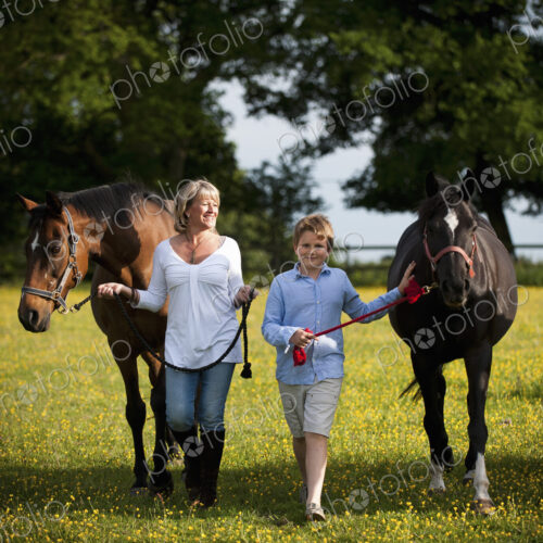 A woman and a boy walking in a field with two horses. A woman and a boy walking in a field with two horses.