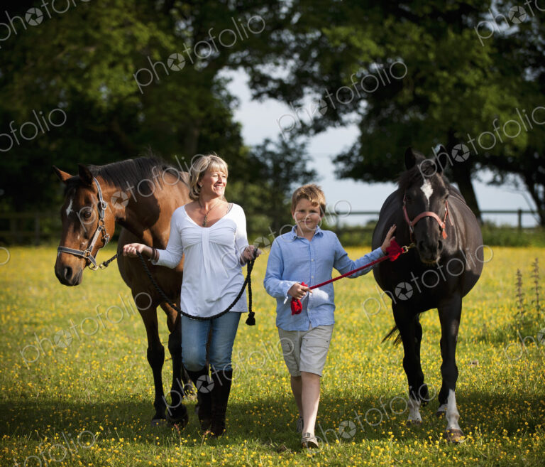 A woman and a boy walking in a field with two horses.